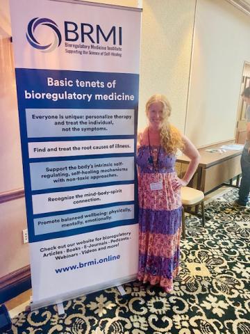 Dr. Sharon Stills stands smiling beside a banner for the Bioregulatory Medicine Institute.